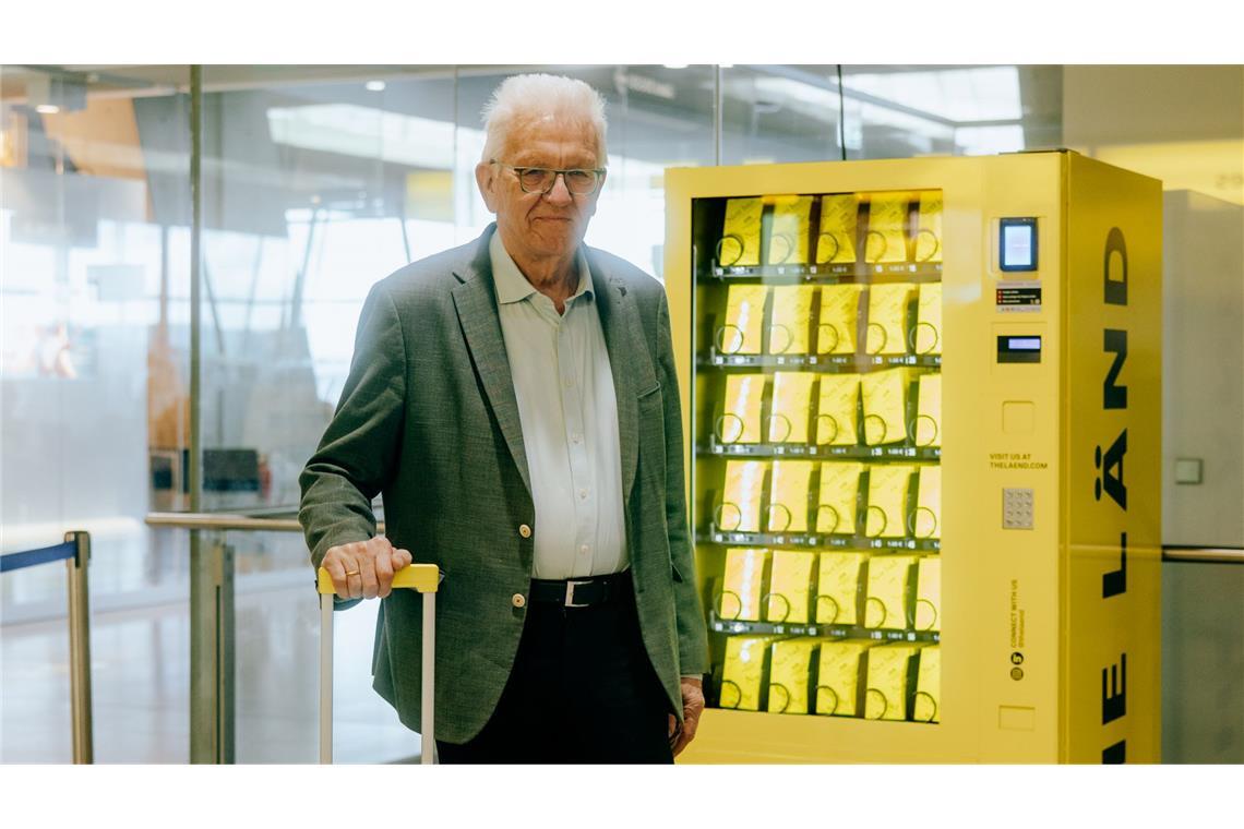 Ministerpräsident Winfried  Kretschmann vor dem „Nett-hier“-Sticker-Automat am Flughafen.