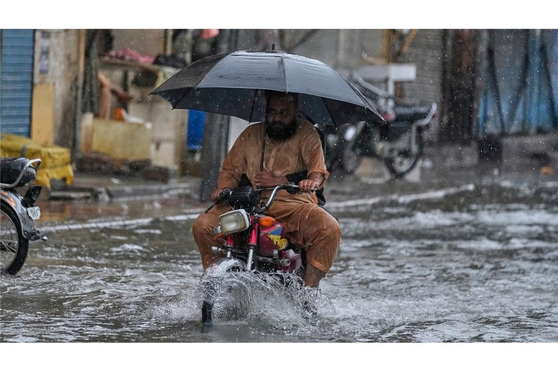 Mit aufgespanntem Regenschirm fährt ein Motorradfahrer waghalsig durch die Monsunfluten.