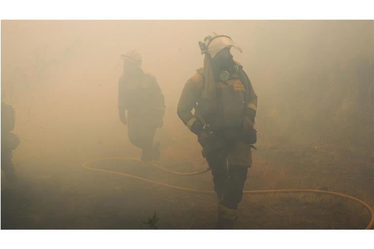 Mitarbeiter der Feuerwehr stehen im Rauch während eines Einsatzes zur Bekämpfung eines Waldbrandes beim  spanischen Crecente.