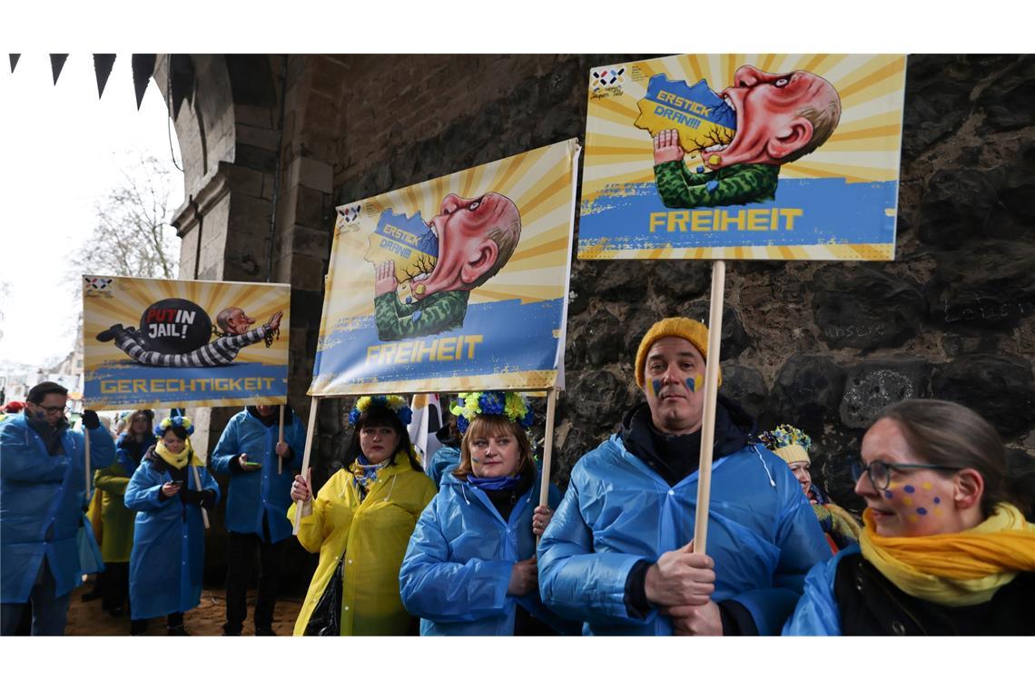 Mitglieder des ukrainischen Hilfsvereins Blau-Gelbes Kreuz halten im Kölner Rosenmontagszug Plakate mit früheren Putin-Darstellungen aus den Zügen in Köln und Düsseldorf hoch.