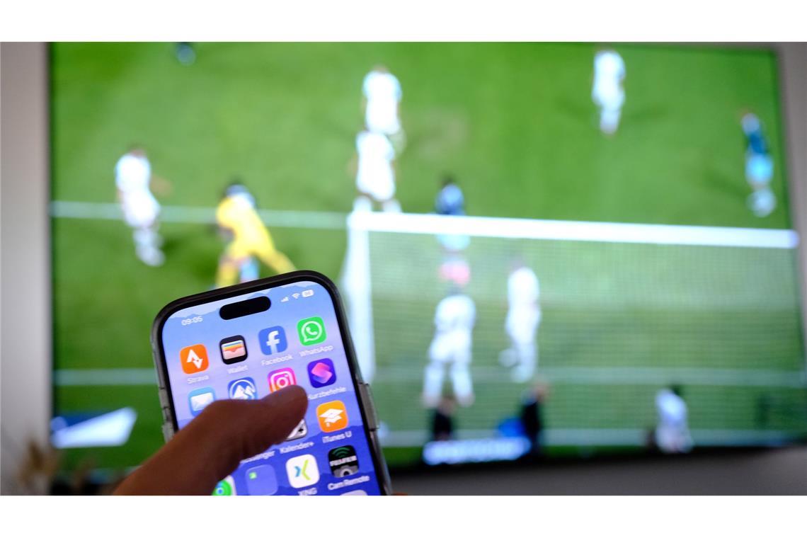 Nebenbei mal daddeln: Während das Fußballspiel läuft, schauen viele Zuschauer nebenbei aufs Handy. (Symbolbild)