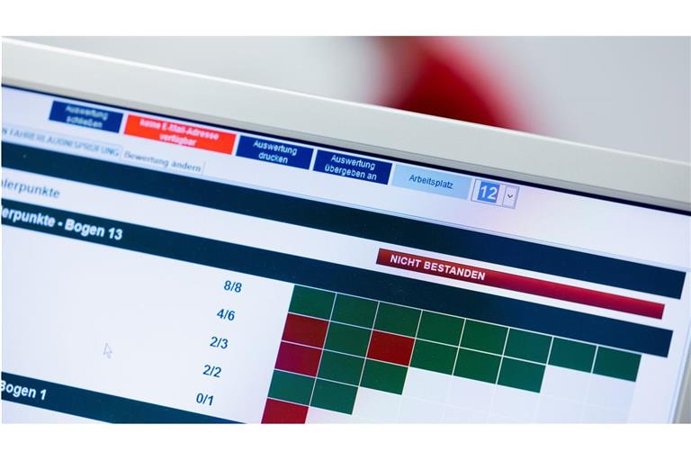 Nicht bestanden“ steht auf dem Monitor eines Prüfers bei der theoretischen Prüfung für den Führerschein, während im Hintergrund Prüflinge die Aufgaben absolvieren.