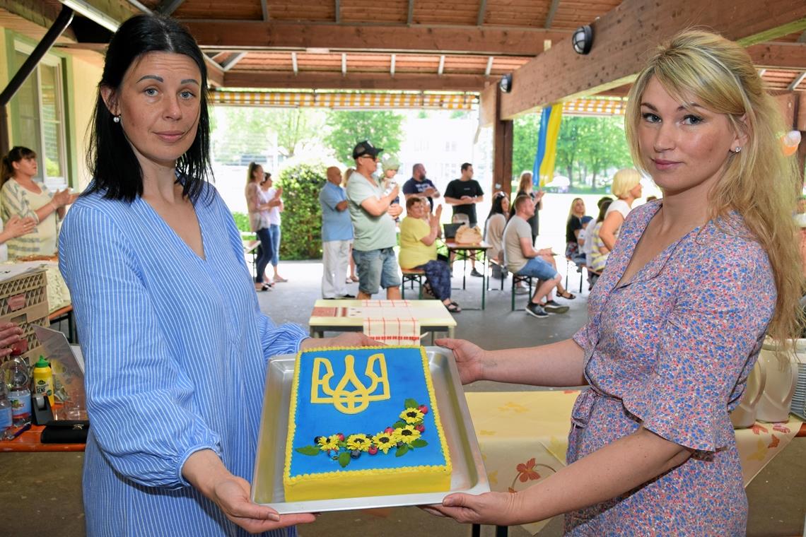 Oksana Kaliuzhna und Natalia Schneider (von links) zeigen die kunstvoll mit dem ukrainischen Wappen dekorierte Torte, die nun für die Gäste angeschnitten wird. Foto: Elisabeth Klaper