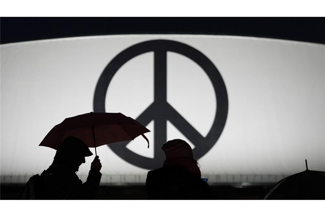 Bilder des Tages Passanten gehen mit Regenschirmen vorbei an einem leuchtenden Peace-Zeichen im strömenden Regen zum Musical-Theater "Stage Theater an der Elbe" im Hafen.