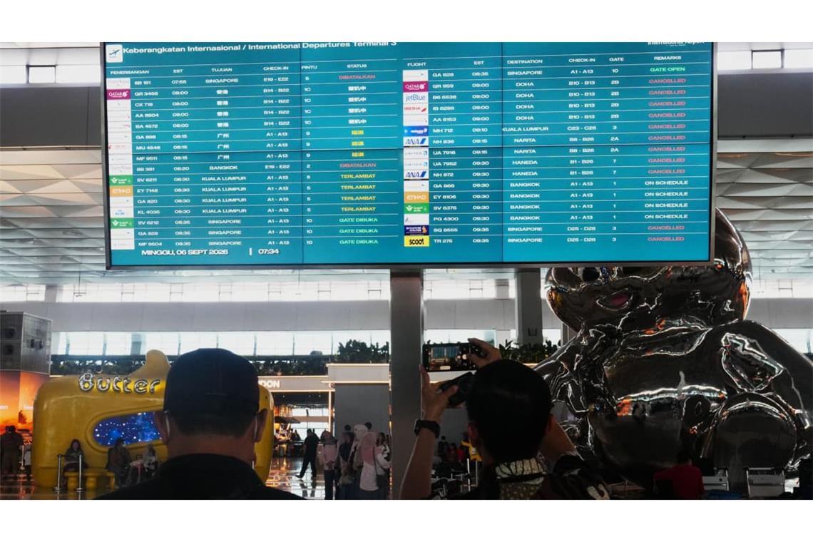 Reisende gehen am internationalen Flughafen Soekarno-Hatta an einer Informationstafel vorbei, auf der Flugausfälle angezeigt werden.