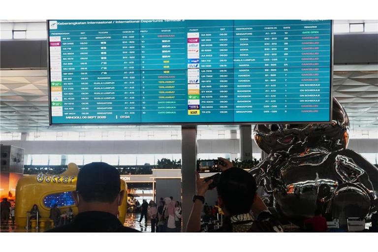 Reisende gehen am internationalen Flughafen Soekarno-Hatta an einer Informationstafel vorbei, auf der Flugausfälle angezeigt werden.