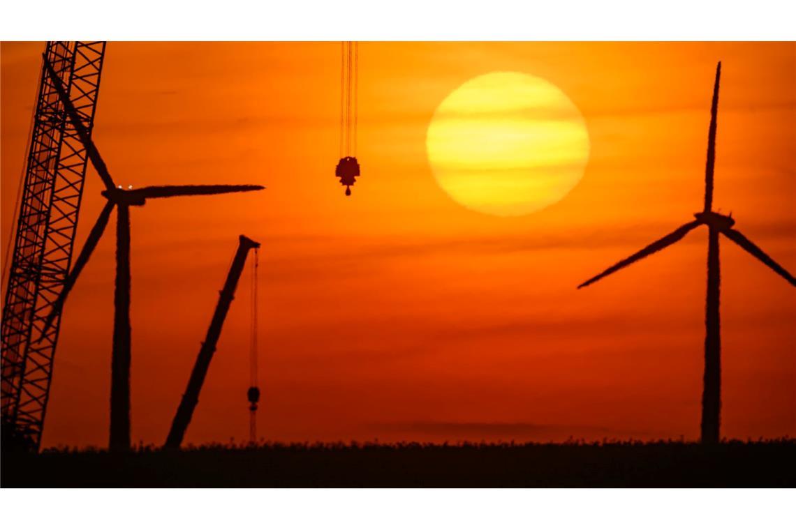 Sonnenaufgang über einer Landschaft mit Windenergieanlagen und einem Kran auf einer Baustelle für ein neues Windrad in Brandenburg.