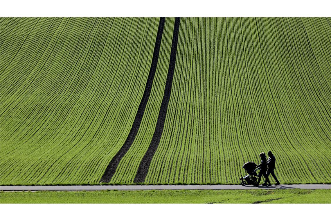 Spaziergänger gehen im Sonnenschein an einem frisch bestellten Feld in Baden-Württemberg vorbei.