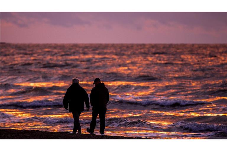 Spaziergänger sind nach Sonnenuntergang am Strand von Warnemünde an der Ostsee unterwegs.