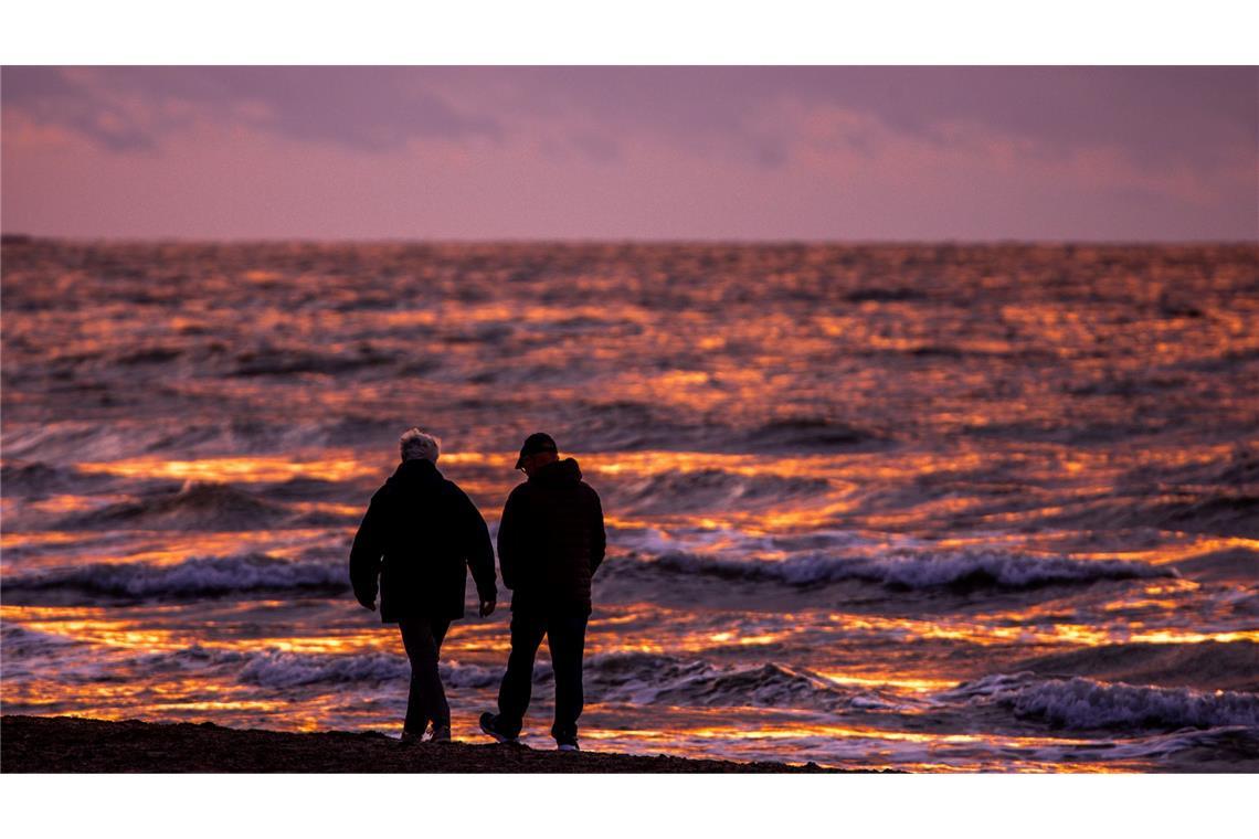 Spaziergänger sind nach Sonnenuntergang am Strand von Warnemünde an der Ostsee unterwegs.