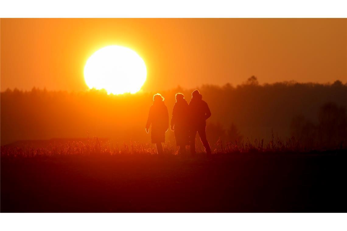 Bilder des Tages Spaziergang an Weihnachten: Menschen gehen im Licht der untergehenden Sonne bei Altheim in Baden-Württemberg durch die Landschaft.