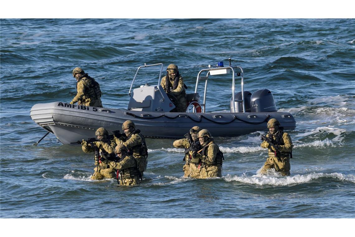 Taucher machen den Anfang und steigen aus dem Wasser auf den schneebedeckten Strand, um den Küstenabschnitt zu sichern.