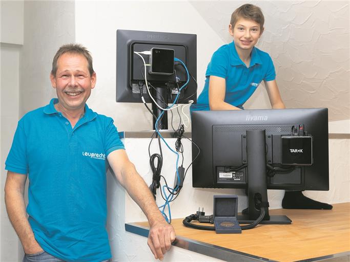 Thomas Leuprecht (links) zeigt mit seinem Sohn Janne (rechts) den Unterschied: Der Bildschirm rechts ist mit seinem „Mini-PC Cable-Caddy“ ausgestattet und die Kabel sind im Gehäuse aufgeräumt – ganz anders als beim Monitor oben links mit dem üblichen Kabelsalat. Foto: J. Fiedler