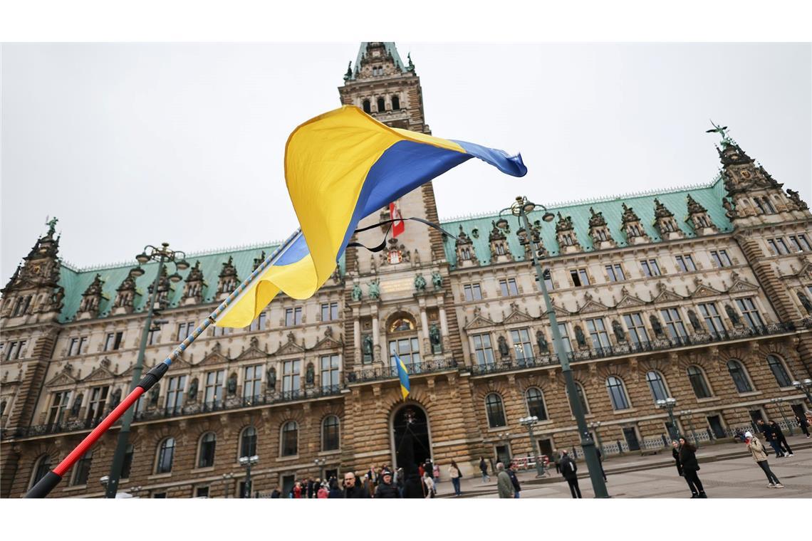 Bilder des Tages Ukraine-Krieg - Dritter Jahrestag. Ein Mann steht mit ukrainischer Fahne und Trauerflor bei der Gedenkminute „Hamburg steht still“ vor dem Rathaus.