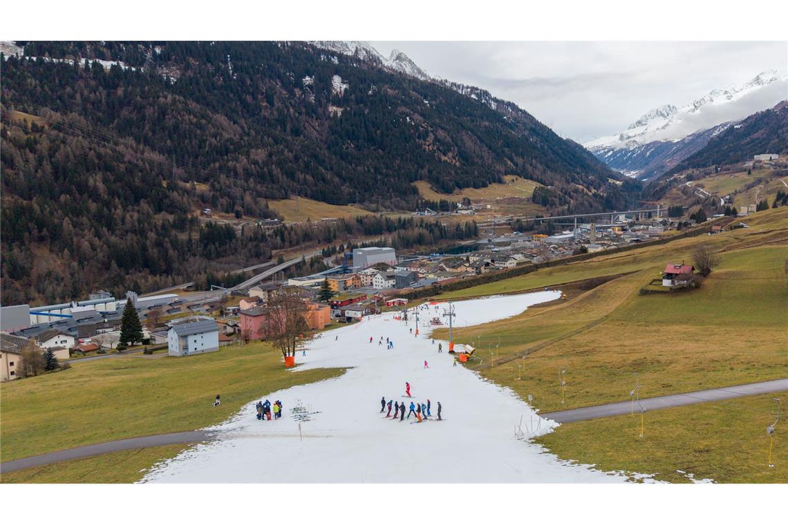 Viel zu warm: Skifahrer fahren auf einer schmalen Piste aus Kunstschnee im Tessin in der Schweiz.