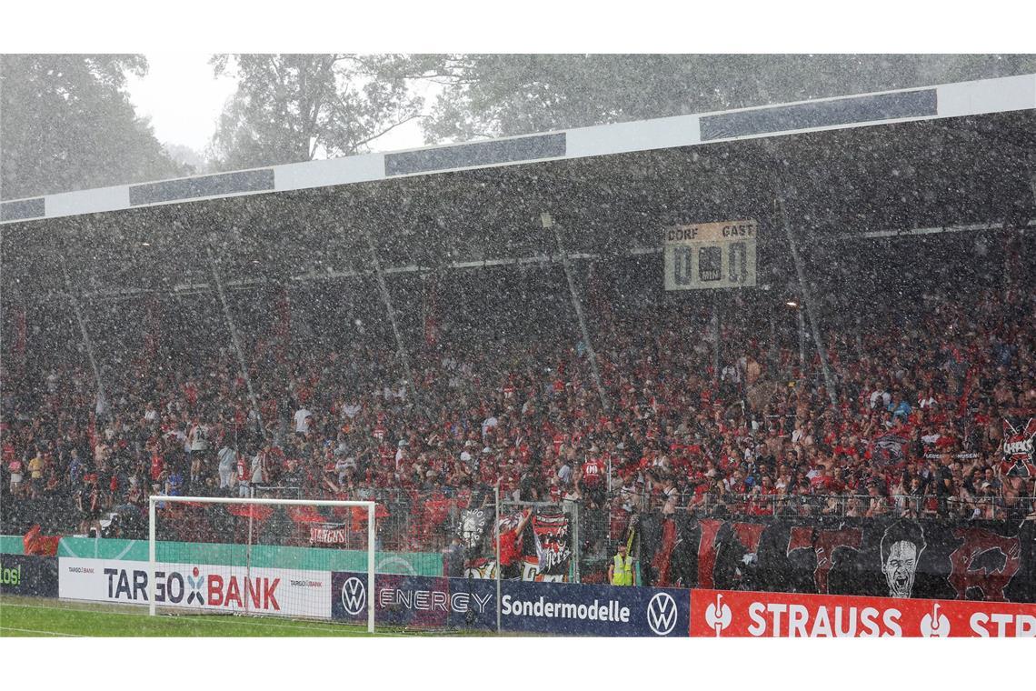 Viele Besucher auf der Zuschauertribüne suchen an diesem regnerischen Tag Schutz vor dem Regen.
