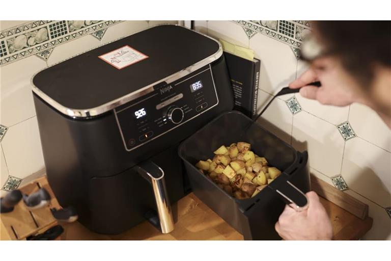 Vielseitig einsetzbar: Ein Mann kocht in seiner Küche mit einer Heißluftfritteuse (Airfryer) ein Gericht aus Kartoffelstücken und gebratenem Hühnerfleisch. (Symbolbild)