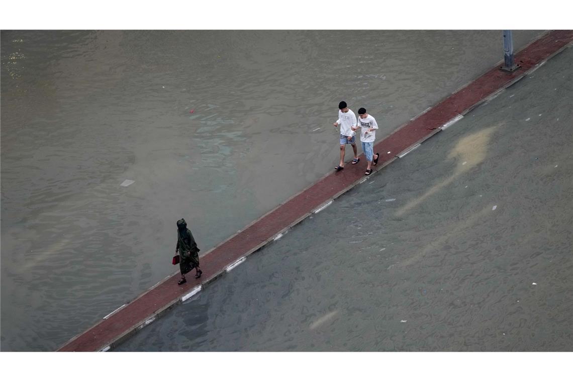Wasser auf der Fahrbahn: Passanten in Dubai suchen auf dem Fahrbahnteiler einen trockenen Weg nach Unwettern