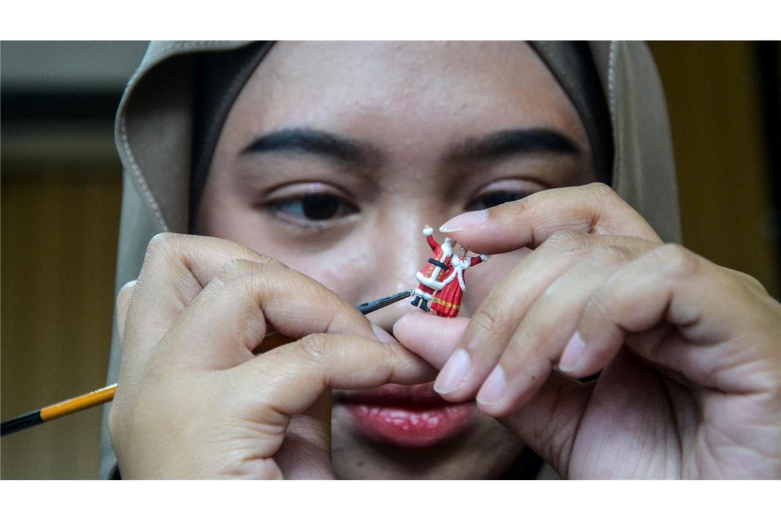 Bilder des Tages Weihnachtsfiguren in Indonesien: eine Frau bemalt eine weihnachtliche Miniaturfigur in einer Werkstatt.