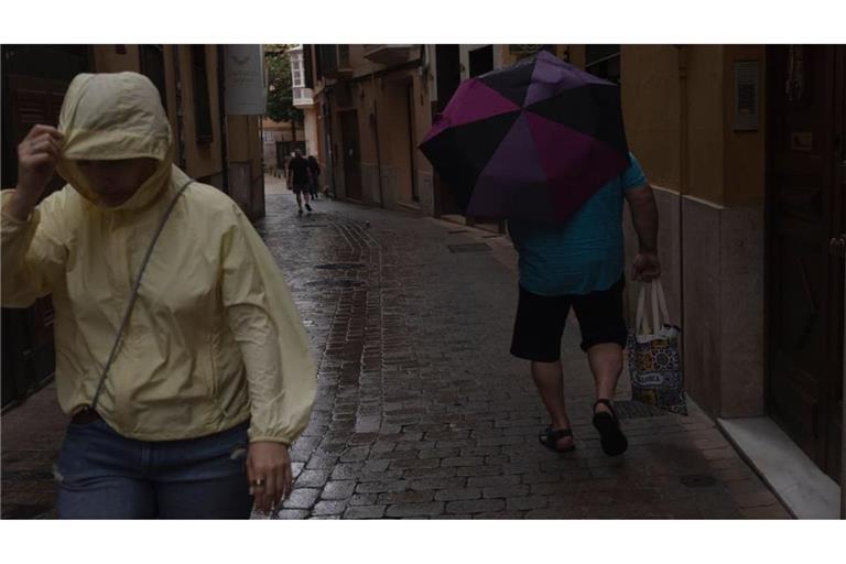 Wetter auf Mallorca: Menschen gehen im Regen durch die Innenstadt von Palma. Der Sturm „Adam“ zieht gerade über die Insel hinweg, und für die Bevölkerung wurde eine rote Warnstufe ausgerufen.