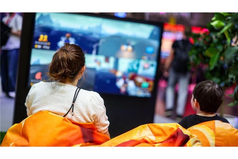 Zwei Besucher der Messe Gamescom sitzen auf Sitzsäcken vor einem Bildschirm und spielen ein Videospiel. Künstliche Intelligenz verändert das Spielen.
