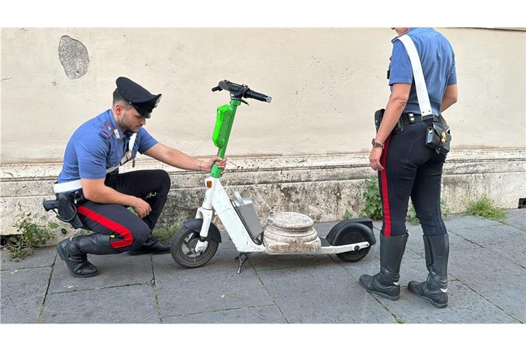 Zwei Carabinieri begutachten den Marmorsockel auf einem elektrischen Leihroller.