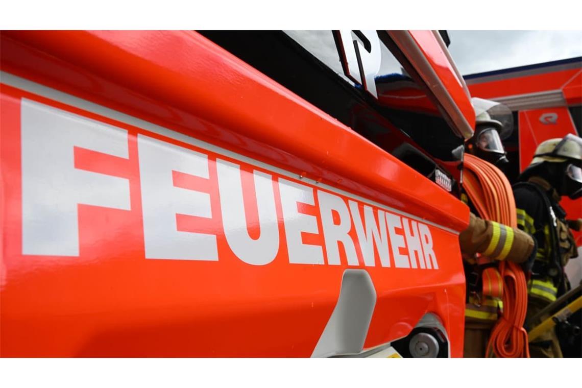 Zwei Feuerwehrleute gehen mit ihrer Ausrüstung zur Brandbekämpfung an einem Einsatzfahrzeug vorbei.