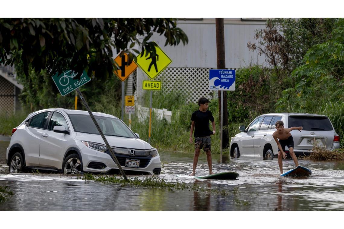 Zwei Jugendliche surfen in Waialua neben einem liegengebliebenen Fahrzeug im Hochwasser.