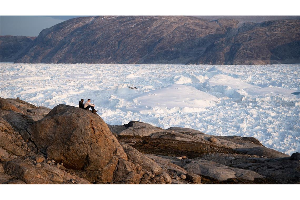 Grönlands Eis schmilzt jedes Jahr um fast 200 Kubikkilometer Zwei Studenten der New York University sitzen auf einem Felsen mit Blick auf den grönländischen Helheim-Gletscher.
